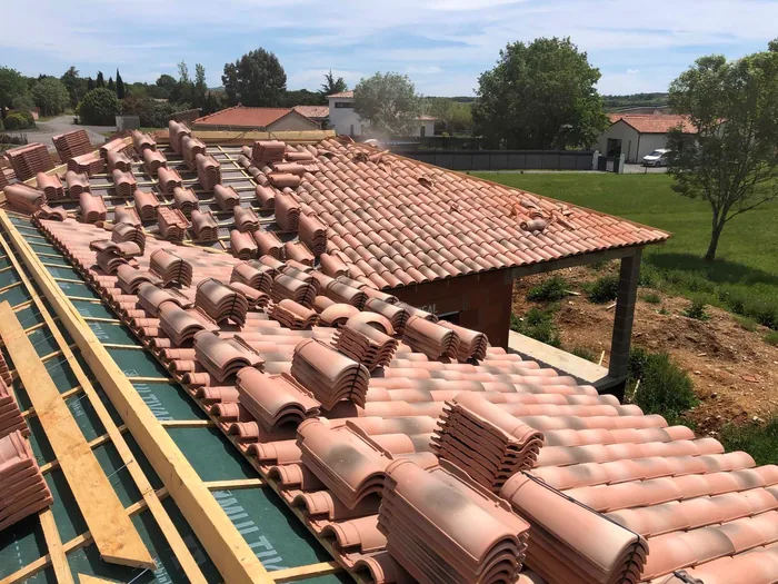 Grande toiture en cours de pose, tuiles empilées sur écran de sous-toiture