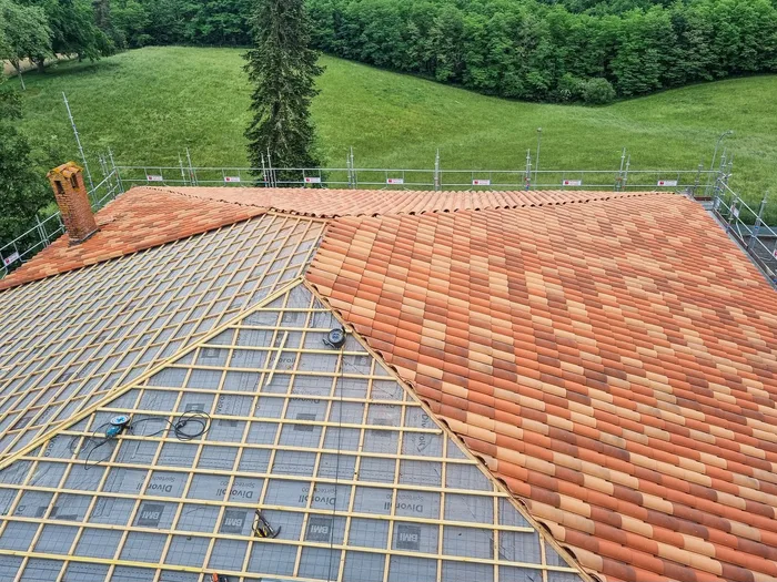 Rénovation de toiture en cours : un pan en tuiles neuves, l’autre au stade de l’écran de sous-toiture et du liteaunage